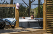 Vrouw geniet van een buitenjacuzzi op een glamping, met houten terras en zonnig, natuurlijk decor.