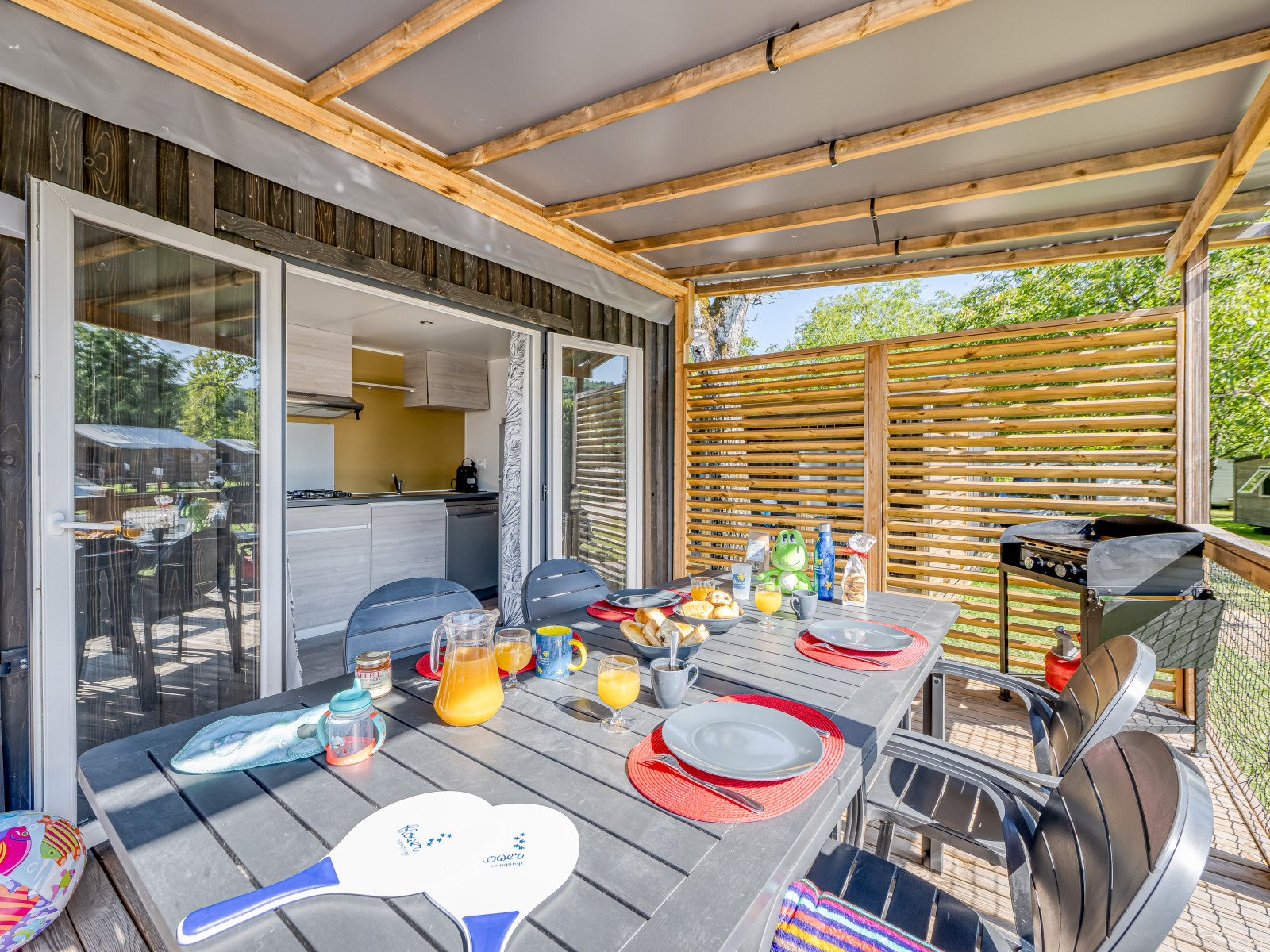Overdekt terras bij glamping met moderne eettafel, ontbijtservies en uitzicht op de natuur.
