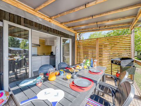 Overdekt glampingterras met ontbijttafel, moderne stoelen en zicht op groen in de natuur.