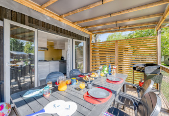 Udendørs spiseområde på glamping med overdækket terrasse, moderne møbler og morgenmadsbord.
