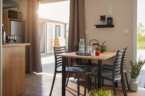 Modern dining area in a glamping accommodation with sunlight, fruit on the table, and a view outside.