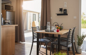 Moderne eethoek in een glamping accommodatie met zonlicht, fruit op tafel en zicht op het terras buiten.
