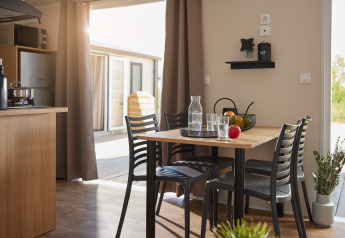 Zona pranzo moderna in un alloggio glamping con luce naturale, frutta sul tavolo e vista sull'esterno.