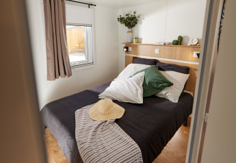 Camera glamping accogliente con letto matrimoniale, cuscino verde, cappello di paglia e luce naturale.