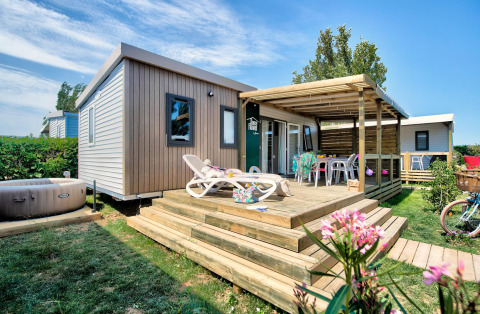 Homeflower PREMIUM Jacuzzi-lodge met ruim houten terras, ligstoelen en een privéjacuzzi in een groene tuin.