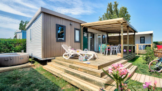 Homeflower PREMIUM Jacuzzi-lodge met ruim houten terras, ligstoelen en een privéjacuzzi in een groene tuin.