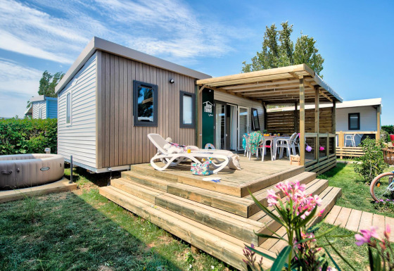 Homeflower PREMIUM Jacuzzi-lodge met ruim houten terras, ligstoelen en een privéjacuzzi in een groene tuin.