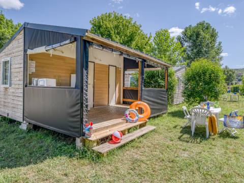 Cabina Mobitoile Standaard con veranda aperta, tavolo da giardino e spazio erboso in ambiente naturale.