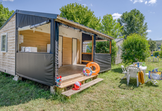 Mobitoile Standaard Hütte mit offener Terrasse, Gartenmöbeln und grünem Rasen unter blauem Himmel.