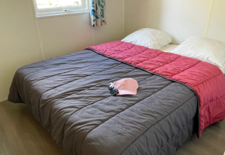 Slaapkamer met tweepersoonsbed in Mobitoile Standaard bij Flower Camping Les Ondines, Frankrijk, met zonnebril en roze pet op het bed.