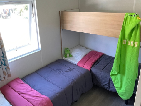 Knusse slaapkamer in een Mobitoile Standaard-hut bij Flower Camping Les Ondines, Frankrijk, met twee bedden en raam.