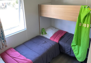 Gemütliches Schlafzimmer in einer Mobitoile Standaard-Hütte im Flower Camping Les Ondines, mit Einzelbetten und Fenster.