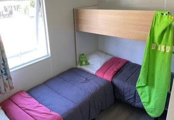 Et hyggeligt soveværelse i en Mobitoile Standaard-hytte på Flower Camping Les Ondines, med enkeltsenge og et lille vindue.