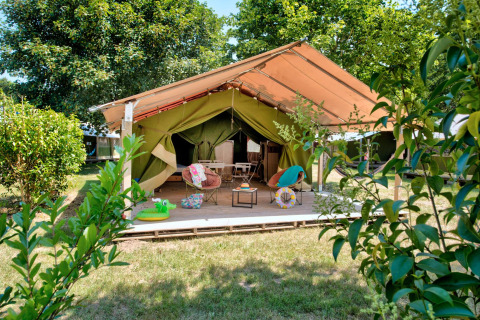 Safari tent Freeflower Standard met open terras, gezellige stoelen en groene, natuurlijke omgeving.