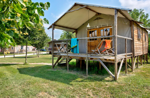 Cabane Lodge Confort, una cabina di legno su palafitte con veranda, sdraio e asciugamani colorati fuori.