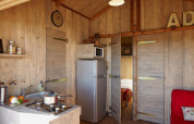 Innenansicht der Cabane Lodge Confort in Flower Camping Les Ondines, Frankreich, mit Küche und Wohnbereich.