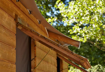 Træhytte med buet tag og åbent vindue i det grønne ved Cabane Lodge Confort, Flower Camping Les Ondines, Frankrig.