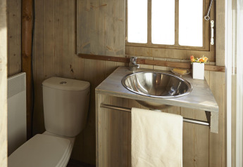 Piccolo bagno in alloggio glamping con pareti in legno, lavandino in acciaio e toilette vicino alla finestra.