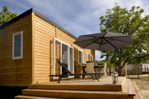 Zonnig terras bij Mobil-Home Premium Met airco, houten huis met tuinmeubels en grote parasol