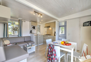 Modern glamping accommodation with a bright kitchen, dining table, grey sofa, and curtained windows.