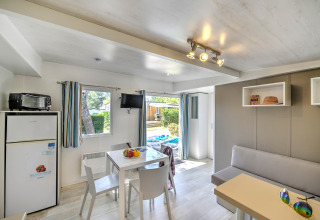 Hébergement glamping lumineux avec table à manger, canapé, réfrigérateur et accès à une terrasse extérieure.