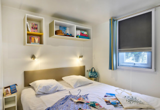 Moderne glamping slaapkamer met dubbel bed, wandrekjes, raam met rolgordijn en kleurrijke accessoires.