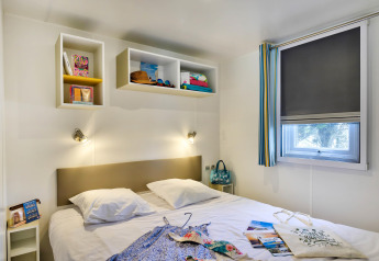 Modernes Glamping-Schlafzimmer mit Doppelbett, Wandregalen, viel Licht und dekorativen Details am Fenster.