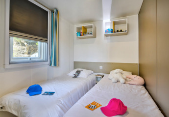 Lichte glampingkamer met twee eenpersoonsbedden, knuffels, kleurrijke petten en een raam.