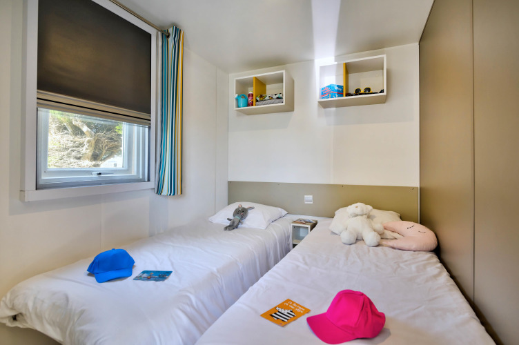 Bright glamping room featuring two single beds, stuffed animals, colorful caps, and a window view.