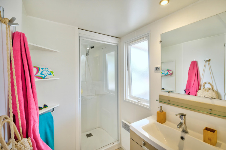 Bagno luminoso in una sistemazione glamping con doccia, finestra, mensole e asciugamani colorati.