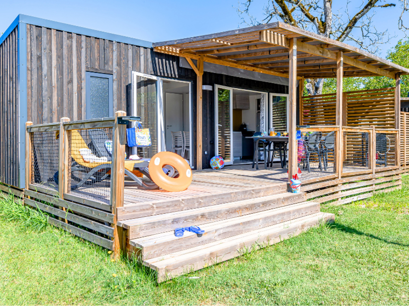 Homeflower Premium cabin met airco, zonnig terras, ligstoelen en groene grasveld rondom.