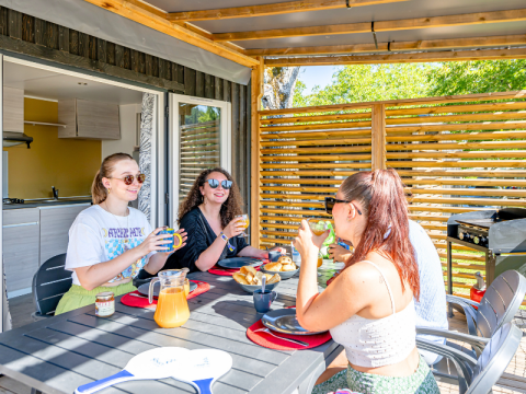 Vier jonge volwassenen genieten van ontbijt op het terras van Homeflower Premium met airco bij Flower Camping Les Ondines.