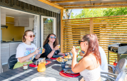 Vier jonge volwassenen genieten van ontbijt op het terras van Homeflower Premium met airco bij Flower Camping Les Ondines.