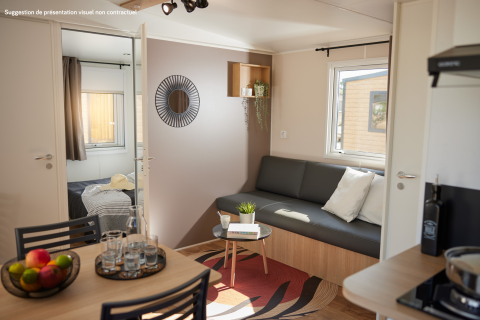 Moderne glampingverblijf met zitruimte, eettafel, fruitschaal, slaapkamer en veel daglicht.