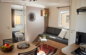 Moderne glampingverblijf met zitruimte, eettafel, fruitschaal, slaapkamer en veel daglicht.