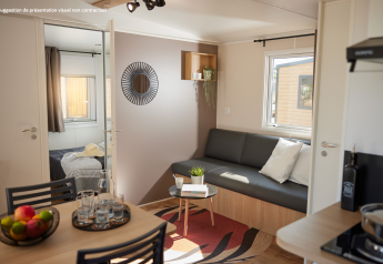 Moderne glampingaccommodatie met woonkamer, eettafel, fruitschaal en slaapkamer met veel licht.
