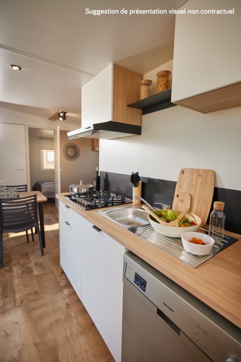 Moderne glampingkeuken met houten werkblad, gaskookplaat, spoelbak, vaatwasser en verse salade.