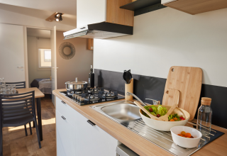 Moderne glampingkeuken met houten werkblad, gaskookplaat, spoelbak, vaatwasser en verse salade.
