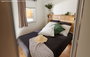 Moderne glamping-indkvartering med komfortabel dobbeltseng, grønne puder og naturligt lys fra vinduet.