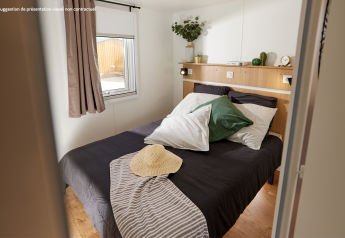 Alojamiento glamping con cama doble, cojines verdes, sombrero sobre la manta y luz natural desde la ventana.