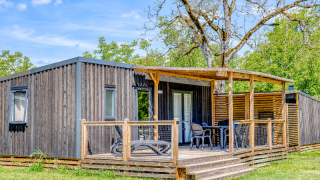 Homeflower Premium met airco: Moderne houten cabin met veranda, tuinset en ligstoelen midden in het groen.