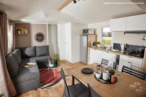 Alloggio glamping moderno con zona living, angolo cottura, tavolo da pranzo e divano grigio.