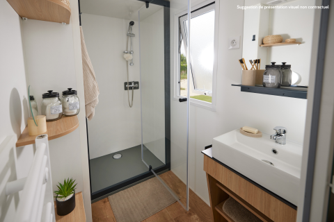 Bagno moderno in una sistemazione glamping con doccia, lavandino, mensole in legno e luce naturale.