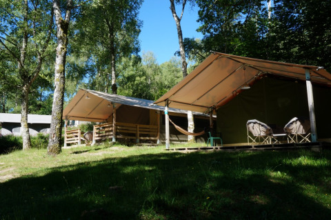 Foto exterior de una tienda safari Freeflower Standaard con porche, hamaca y sillas en un bosque.
