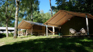 Foto exterior de una tienda safari Freeflower Standaard con porche, hamaca y sillas en un bosque.
