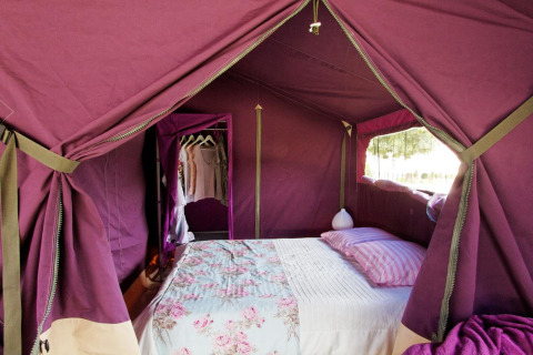 Interior de tienda safari acogedora con cama doble y perchero en Freeflower Standaard, Flower Camping La Plage, Francia.