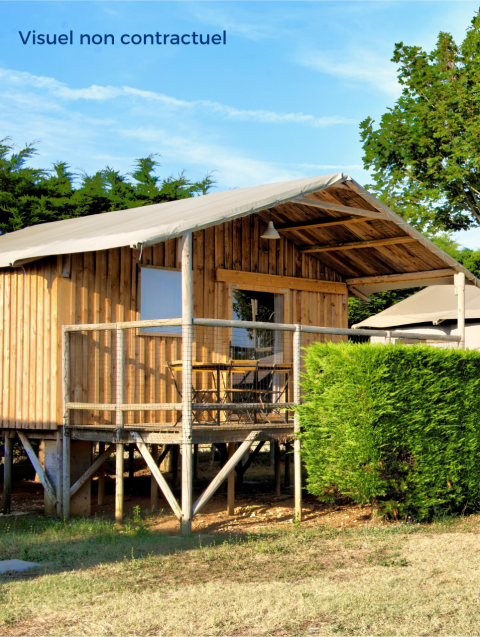 Außenansicht der Cabane Lodge Standaard, eine erhöhte Holzhütte mit Terrasse, Bäumen und Hecke.