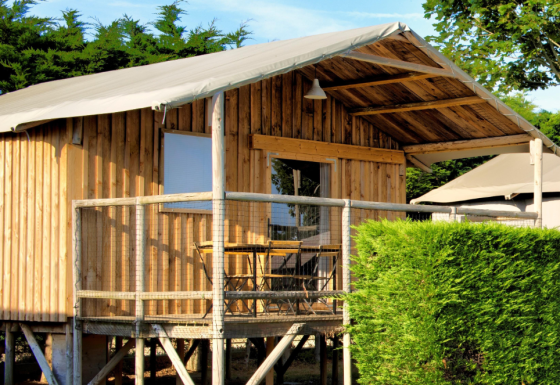 Udendørsbillede af Cabane Lodge Standaard, en hævet træhytte med terrasse, grønne buske og himmel.