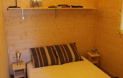 Interior of Cabane Lodge Standaard at Flower Camping La Plage, France, featuring a cozy bed and wood walls.