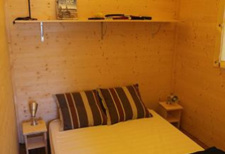 Interiør af Cabane Lodge Standaard ved Flower Camping La Plage i Frankrig med dobbeltseng og trævægge.